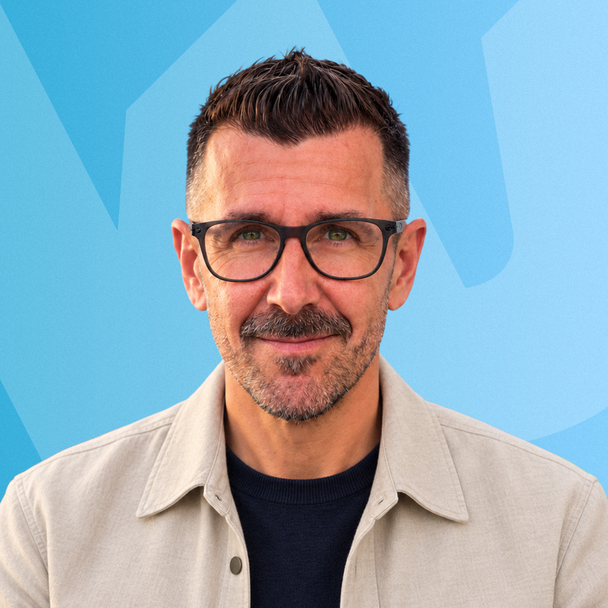 Portrait de Jeff Blanchet sur fond bleu, portant une veste beige et des lunettes noires