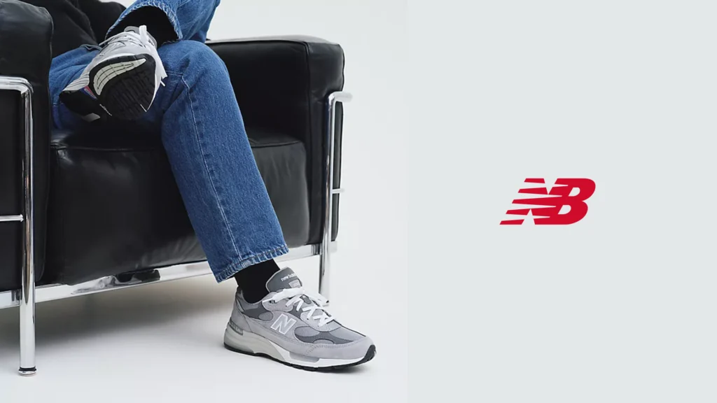 Grey New Balance 992 shoes, jeans and black socks in a black armchair, with the New Balance logo on the right.